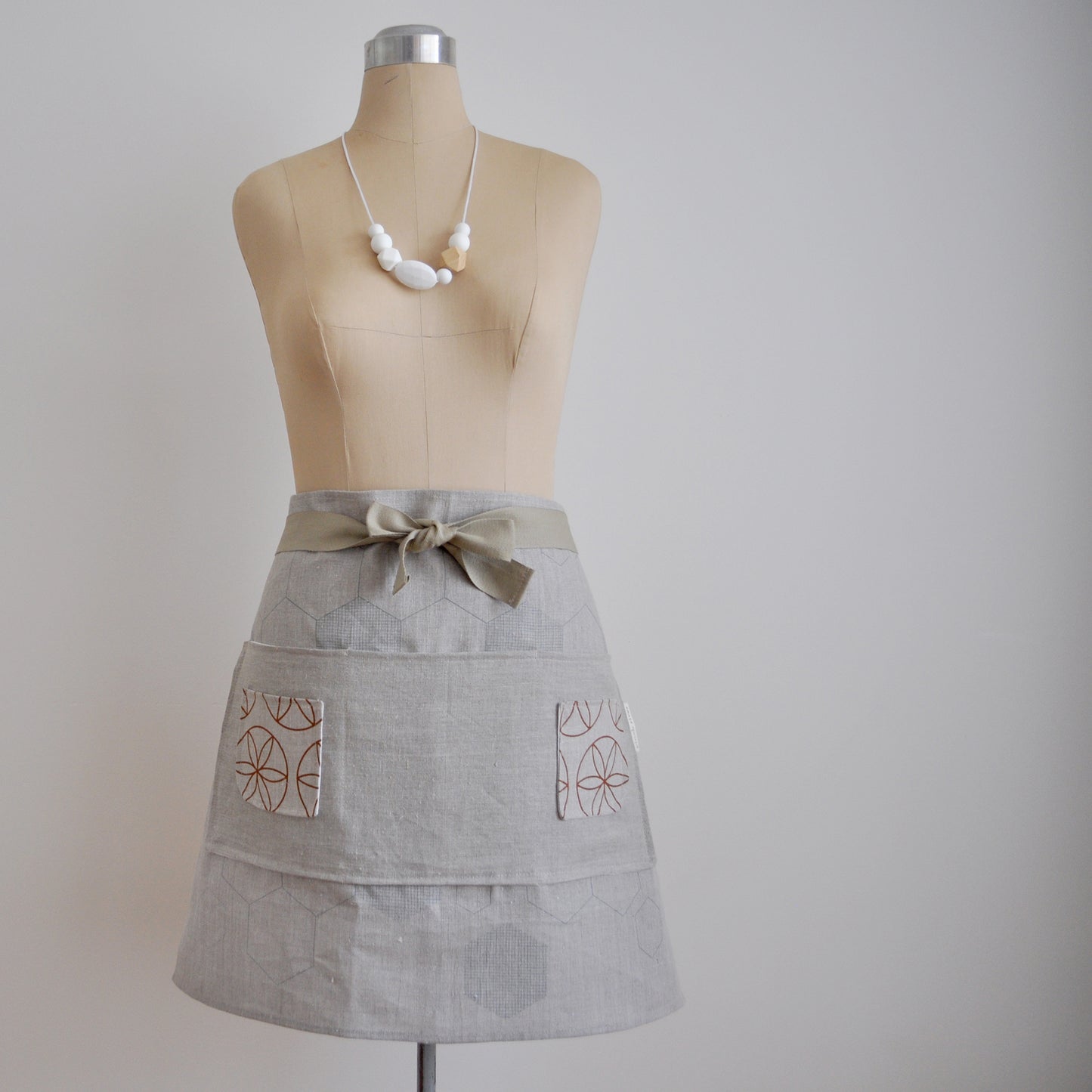 Pinch River waist apron / half apron No. 2 with pockets, on dressmakers dummy against a plain background. Front View.