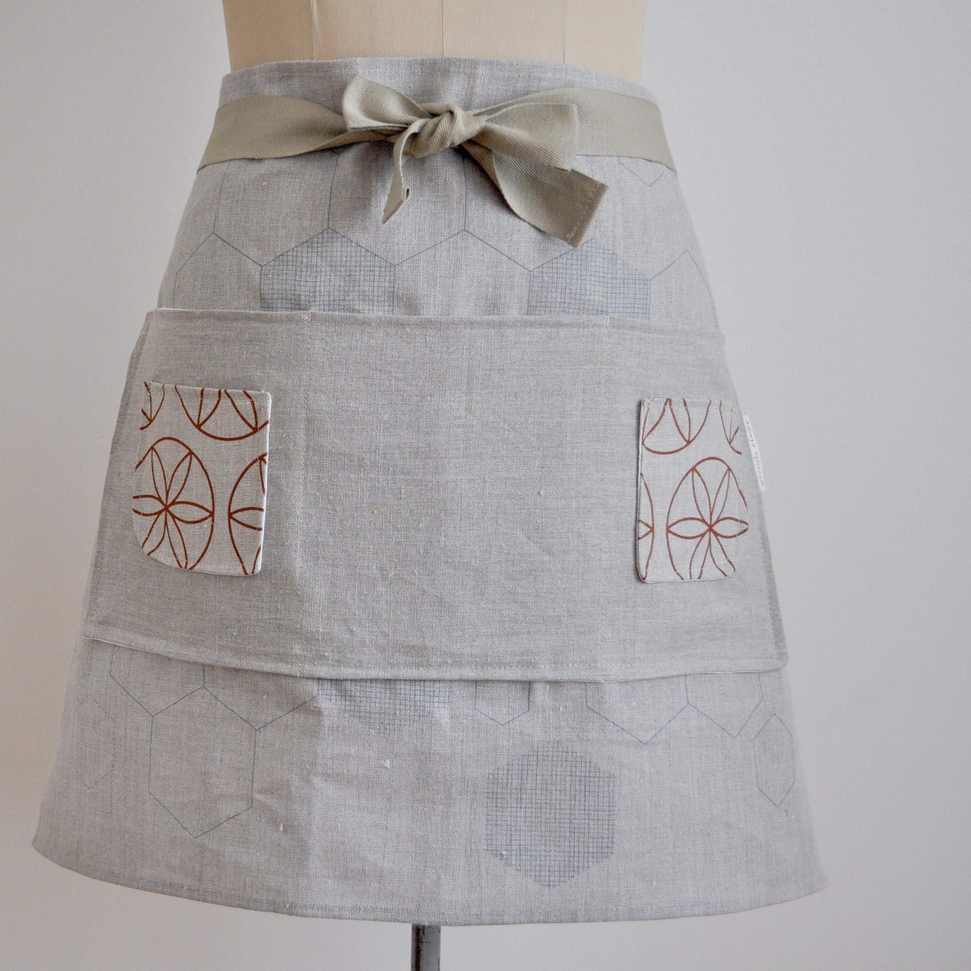 Pinch River waist apron / half apron No. 2 with pockets, on dressmakers dummy against a plain background. Front View. Close-up.