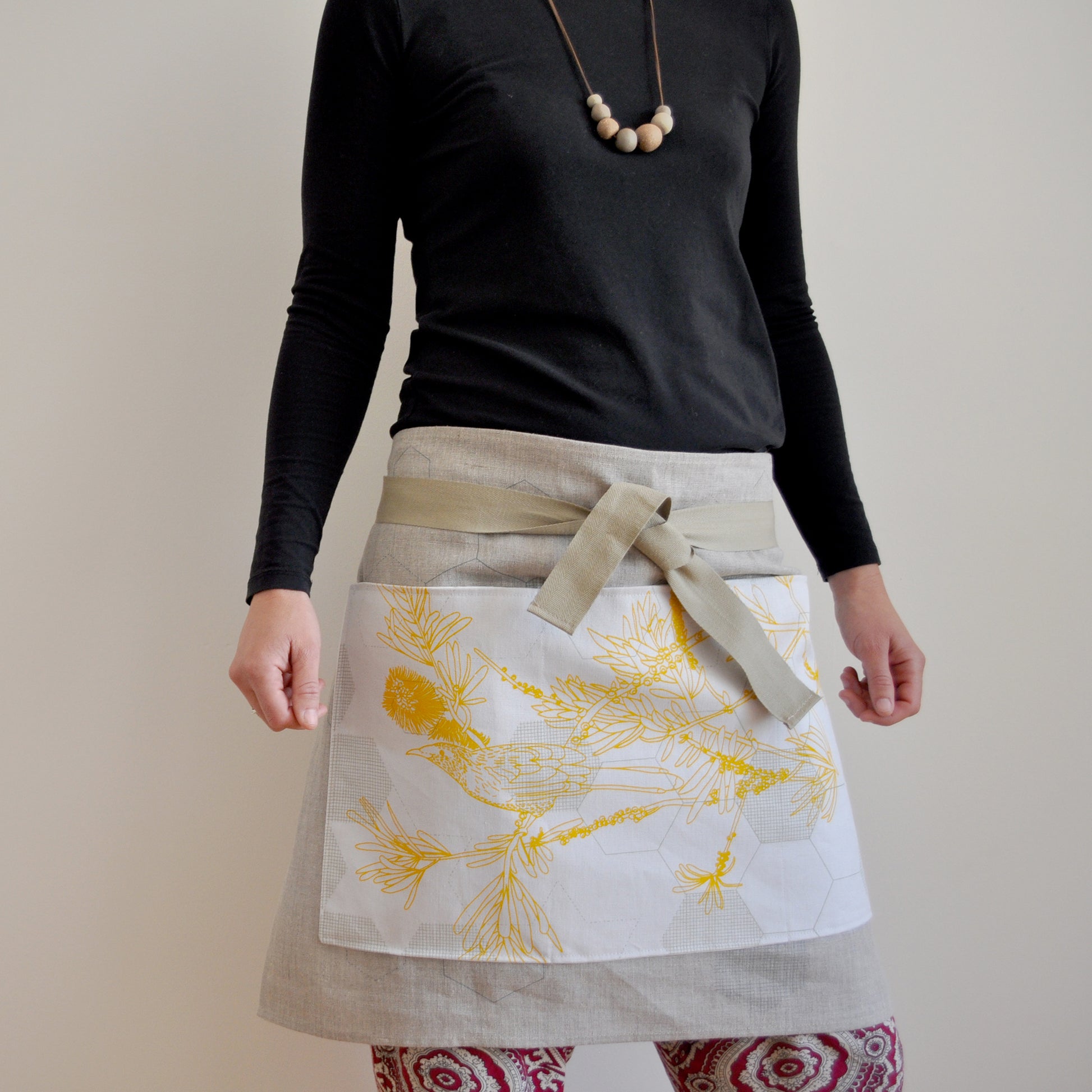 Model wearing Pinch River waist apron / half apron No. 4 with pockets, against a plain background. Front View. Pose #2