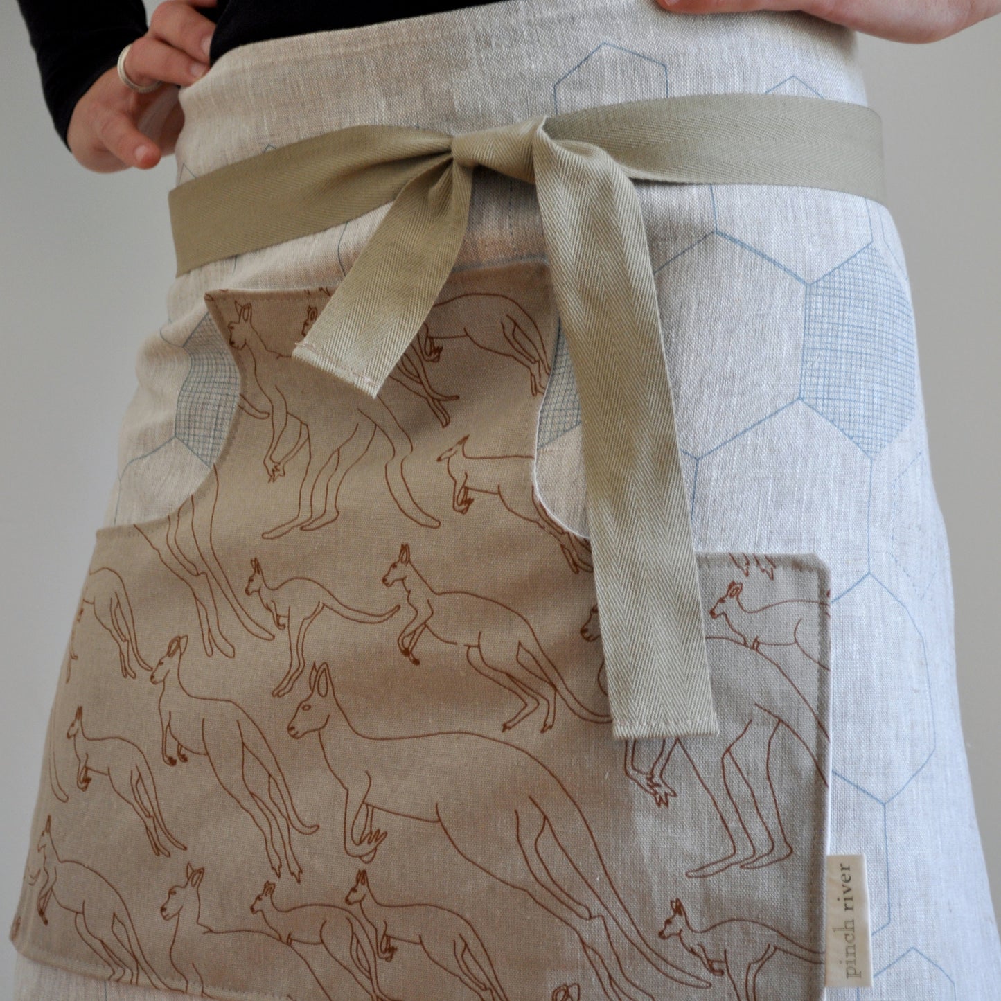 Model wearing Pinch River waist apron / half apron No. 5 with pockets, against a plain background. Front View. Close-up
