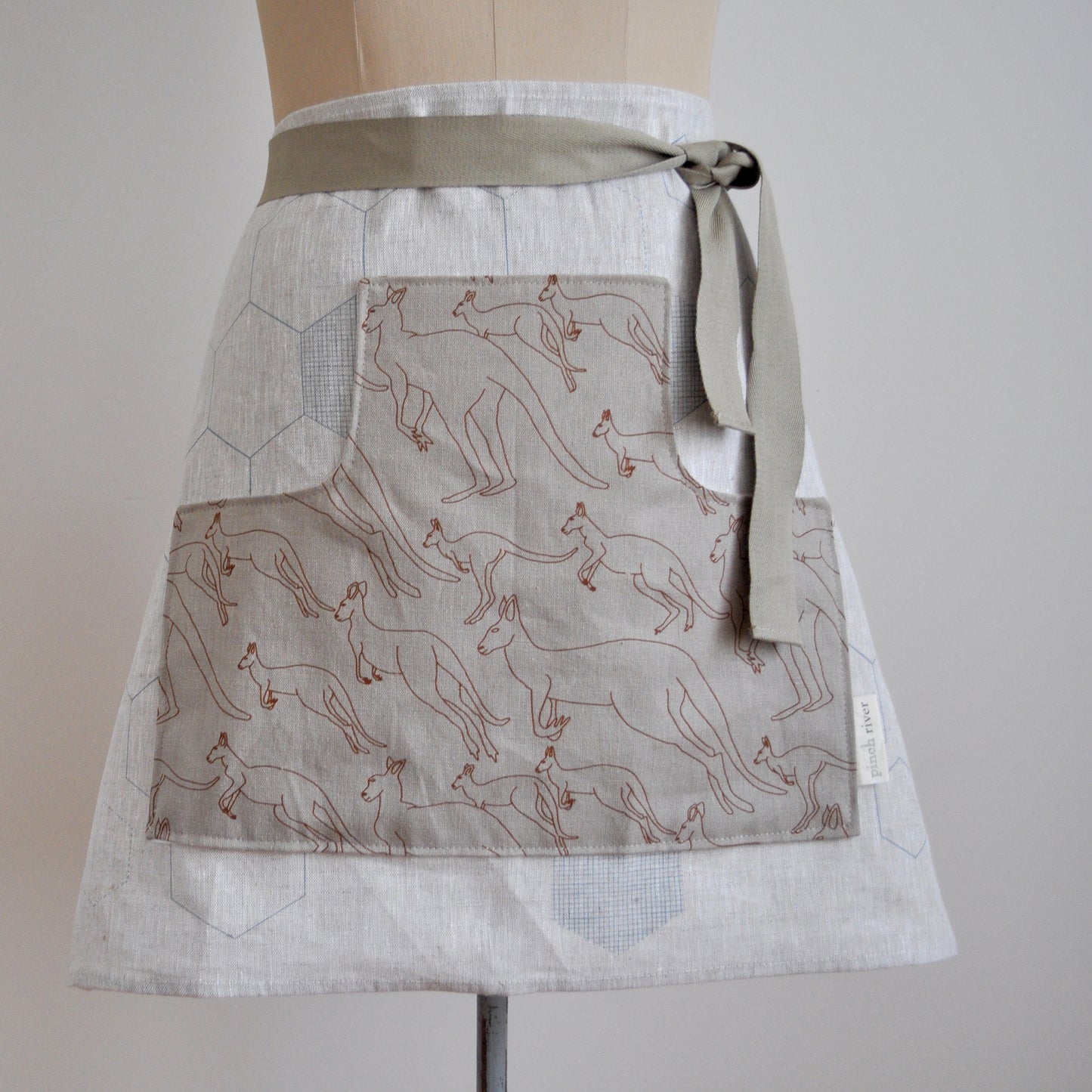 Pinch River waist apron / half apron No. 5 with pockets, on dressmakers dummy against a plain background. Front View. Close-up.