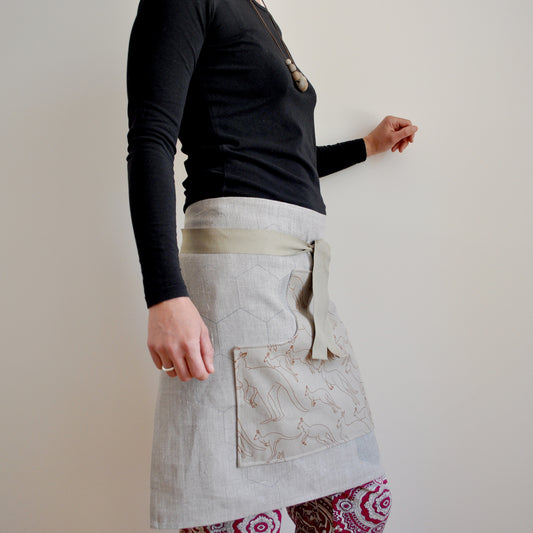 Model wearing Pinch River waist apron / half apron No. 6 with pockets, against a plain background. Side View.