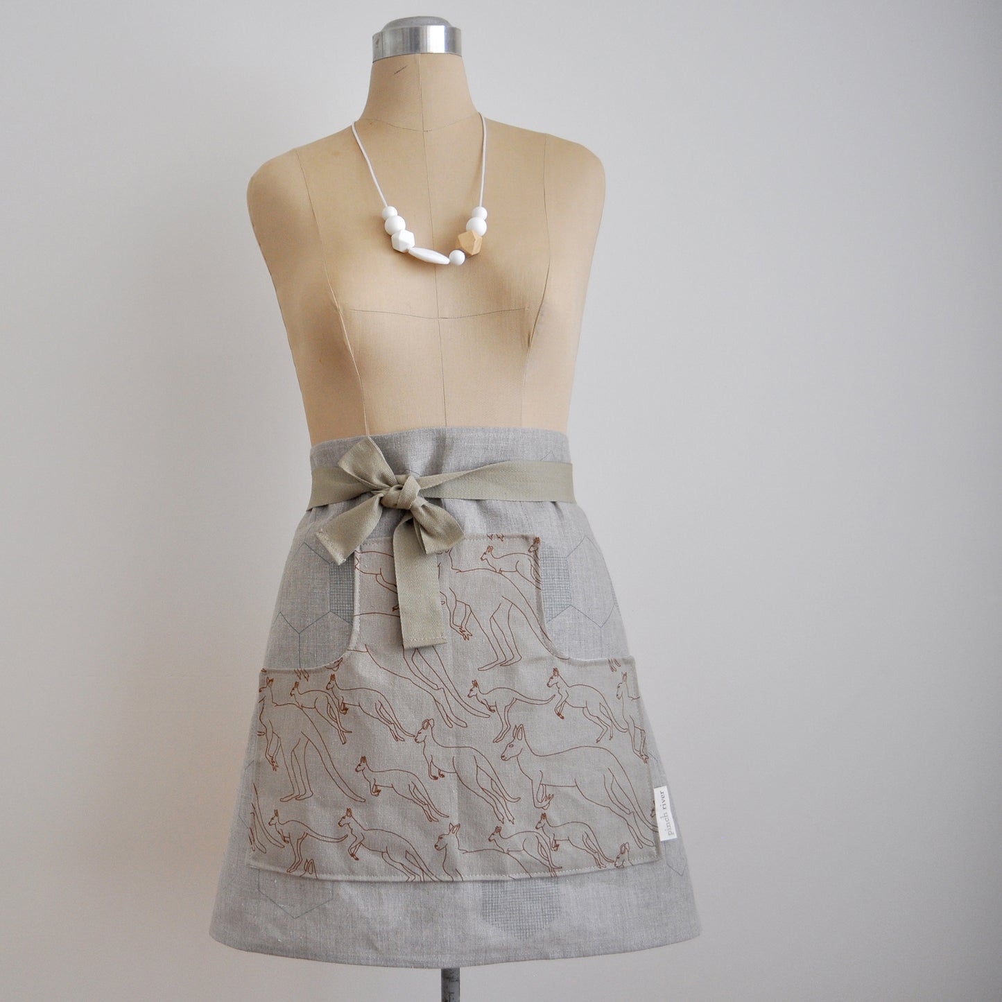 Pinch River waist apron / half apron No. 6 with pockets, on dressmakers dummy against a plain background. Front View.