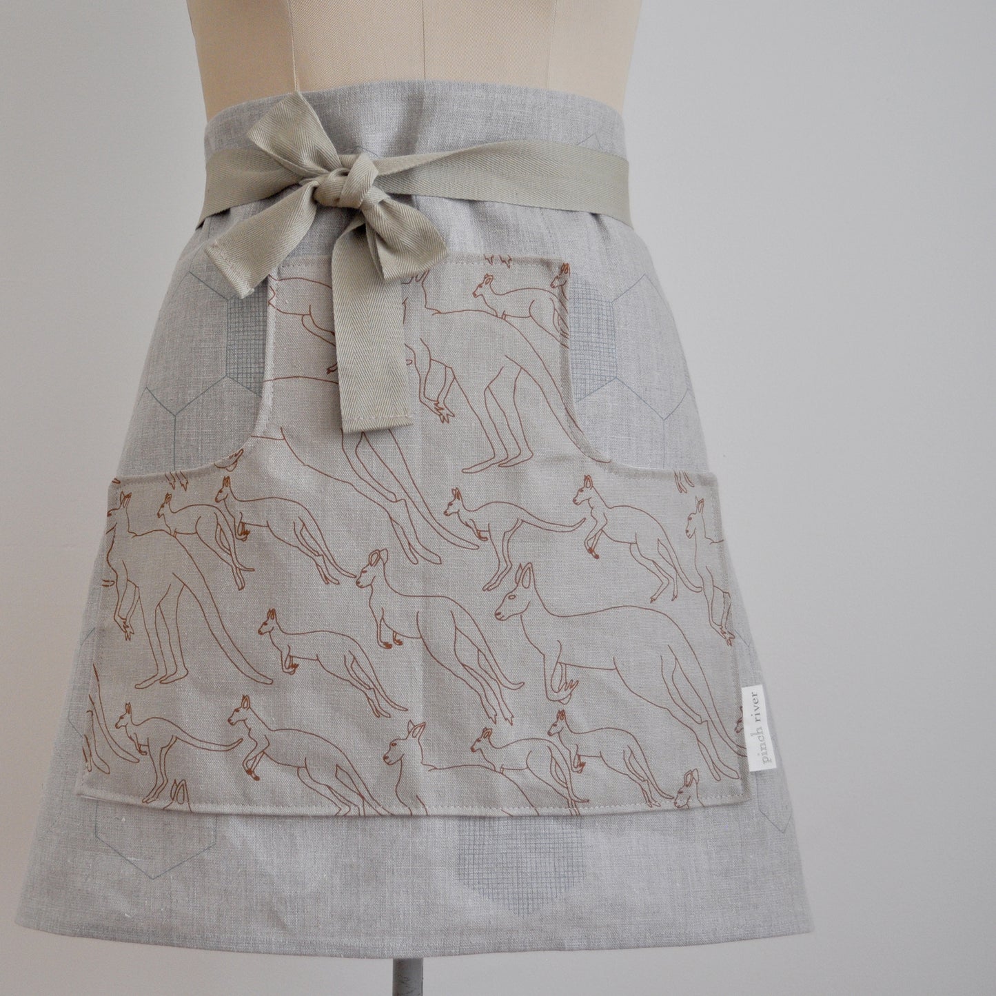 Pinch River waist apron / half apron No. 6 with pockets, on dressmakers dummy against a plain background. Front View. Close-up.