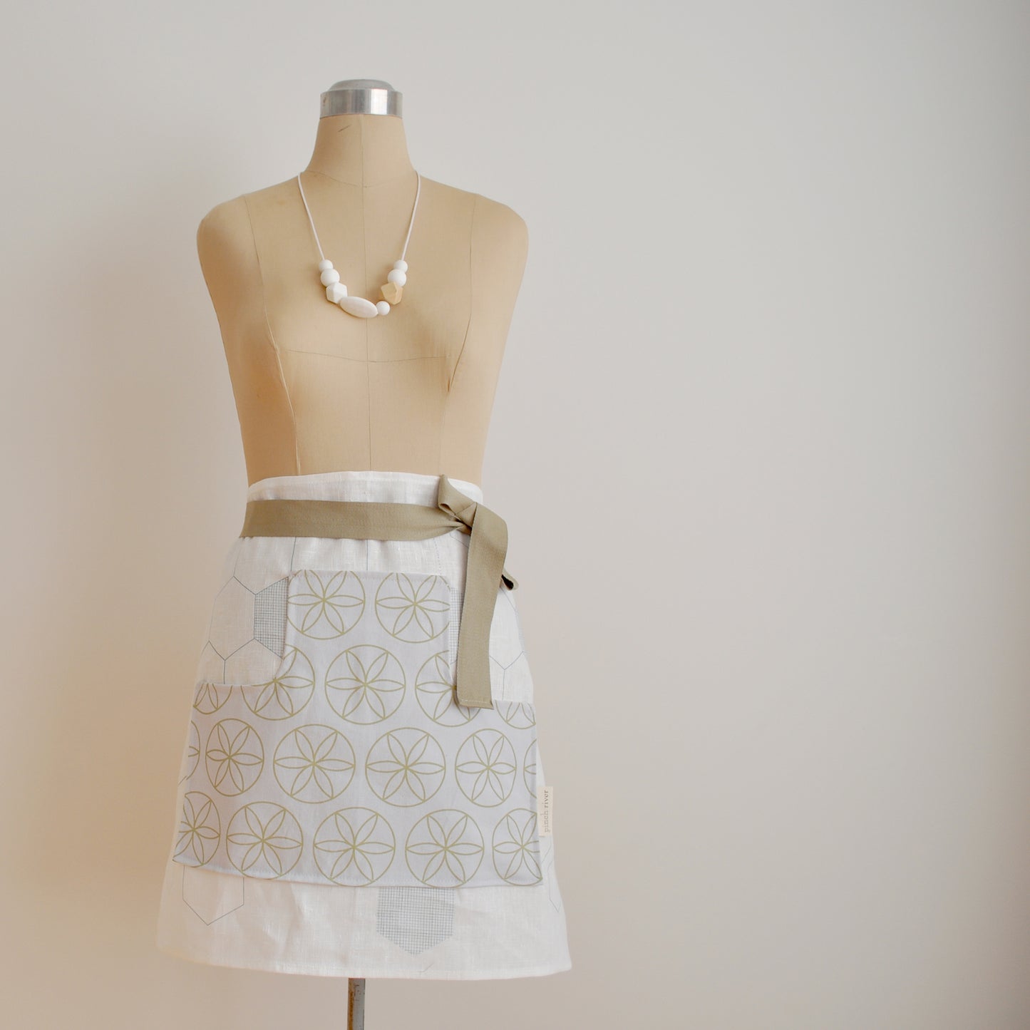 Pinch River waist apron / half apron No. 7 with pockets, on dressmakers dummy against a plain background. Front View.