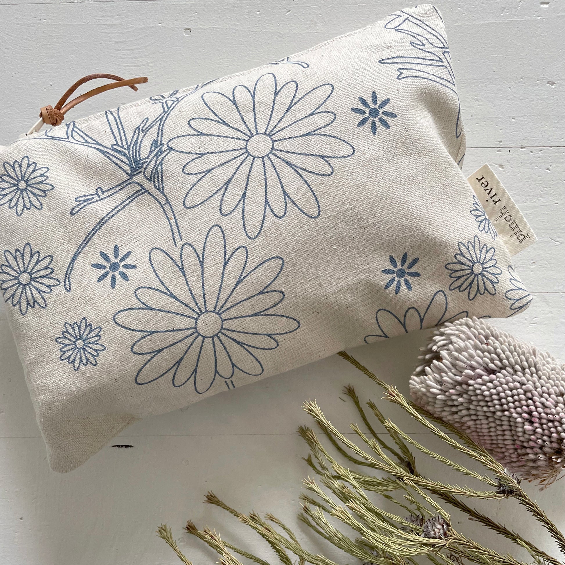 Pinch River zipper pouch featuring Brachycomb print in Horizon Blue (colourway 1). Top view. Product image is styled with Australian native flora.