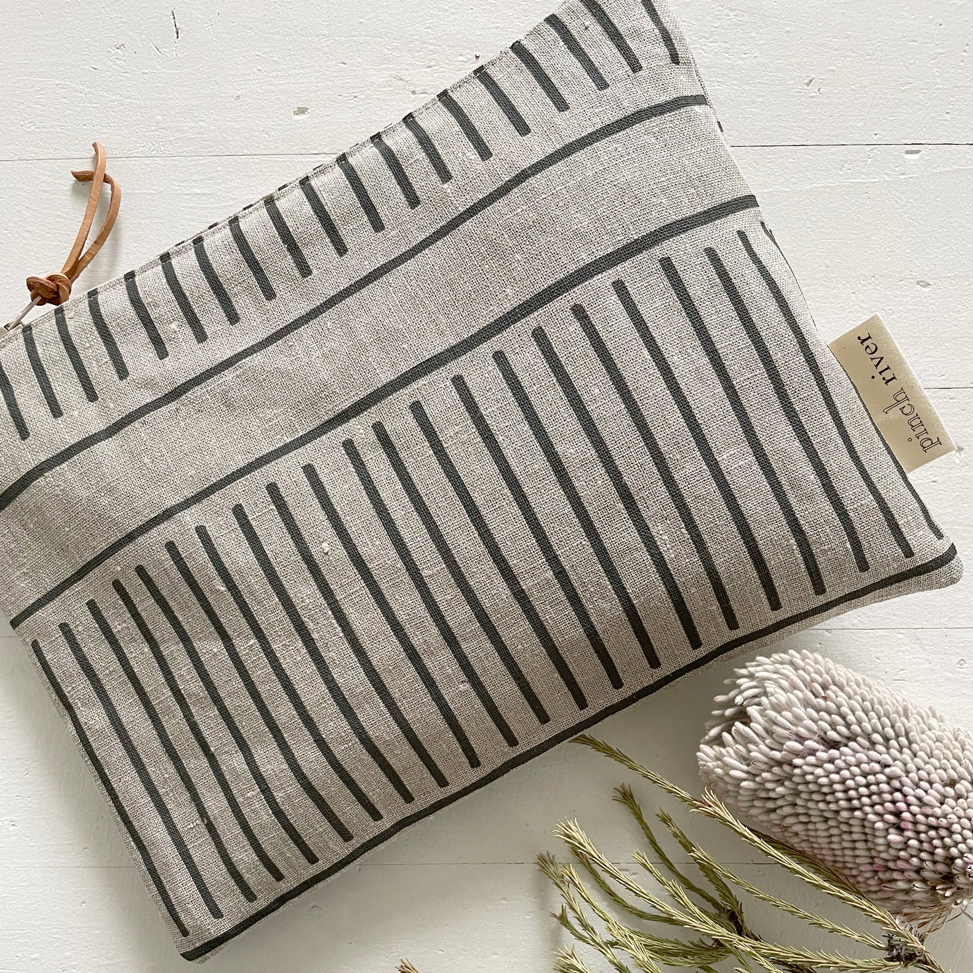 Pinch River zipper pouch featuring Corduroy Pathway print in Gey Bark (colourway 2). Top view. Product image is styled with Australian native flora.