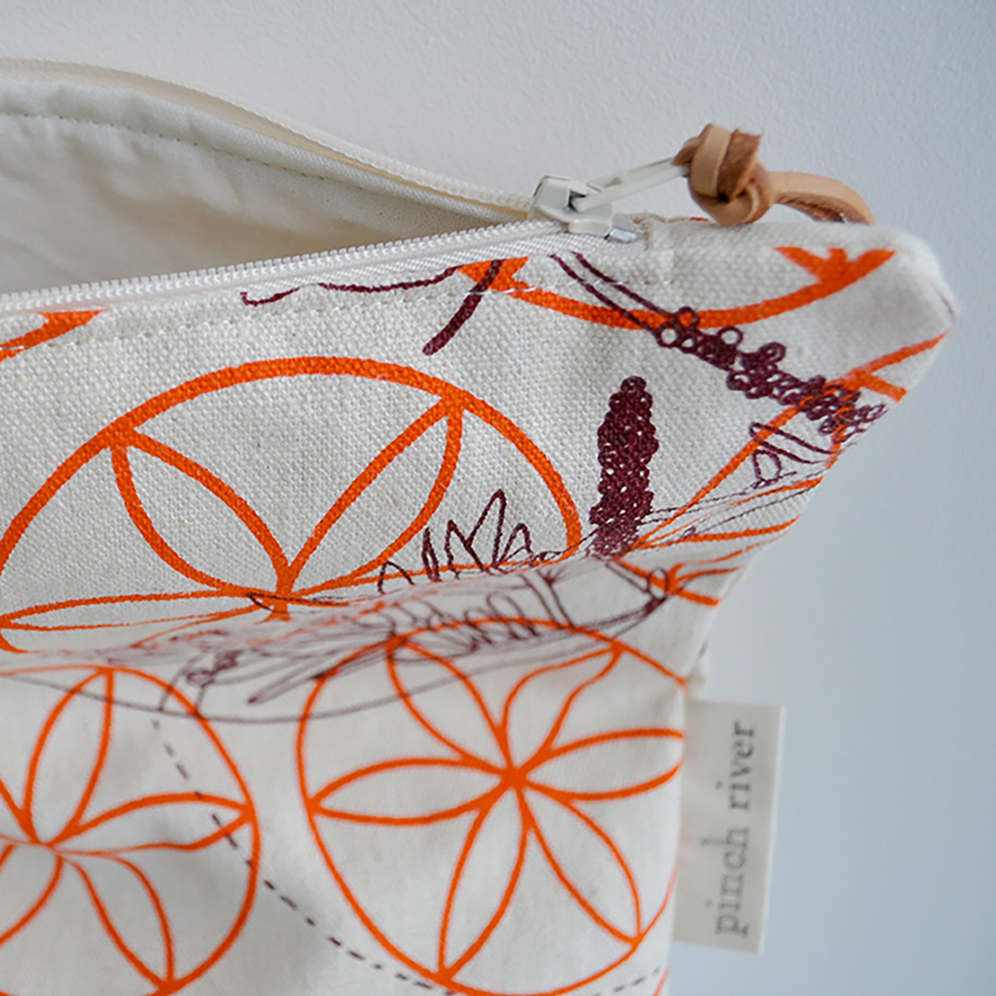 Pinch River zipper pouch featuring Wattle Bird in the Bottle Brush print in Wine Berry (colourway 1) overprinted with Flower of Life print in Fiery Orange (colourway 3). Side view with zipper opened to show the pouch is fully lined.