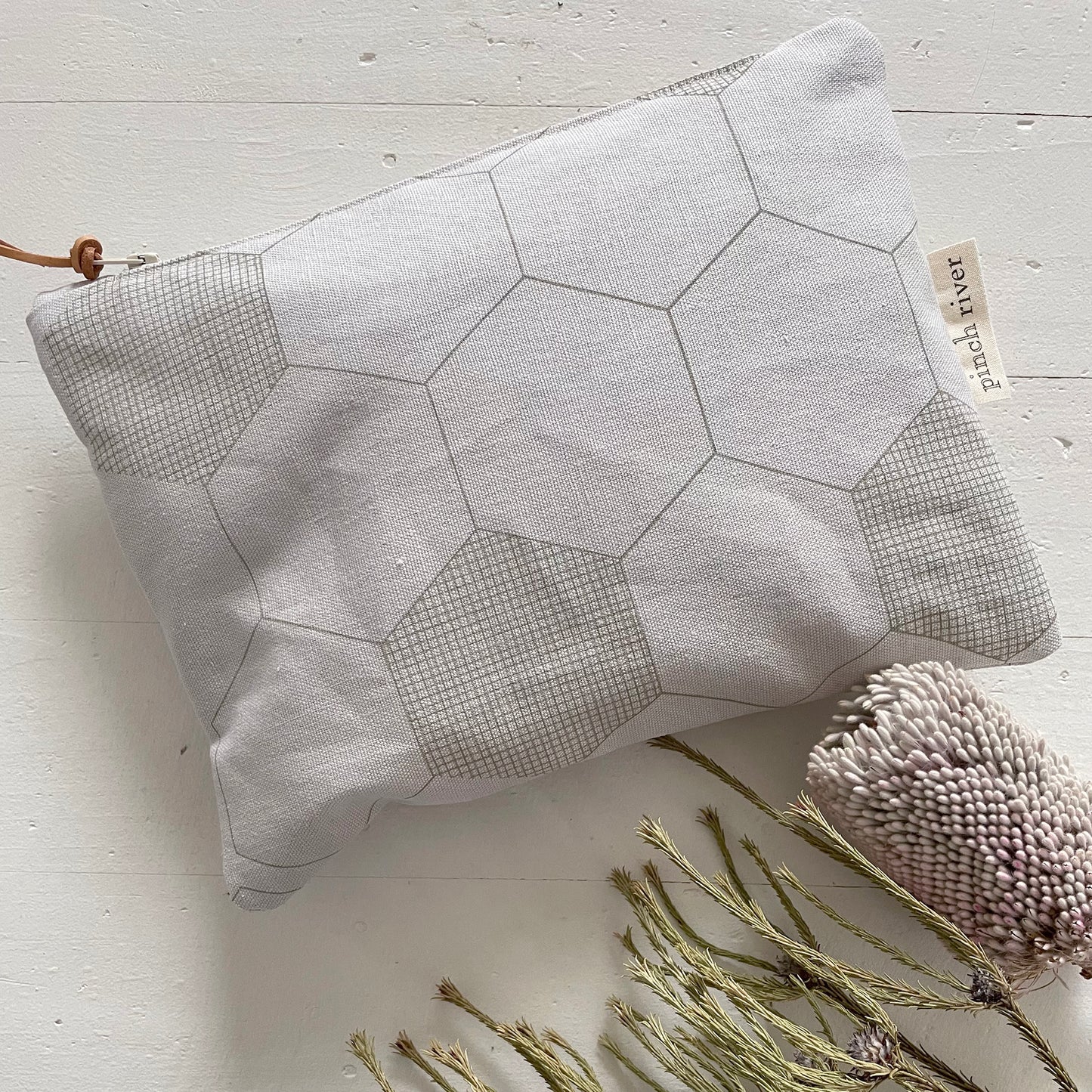 Pinch River zipper pouch featuring Honeycomb print in Moss Green (colourway 1). Top view. Product image is styled with Australian native flora.
