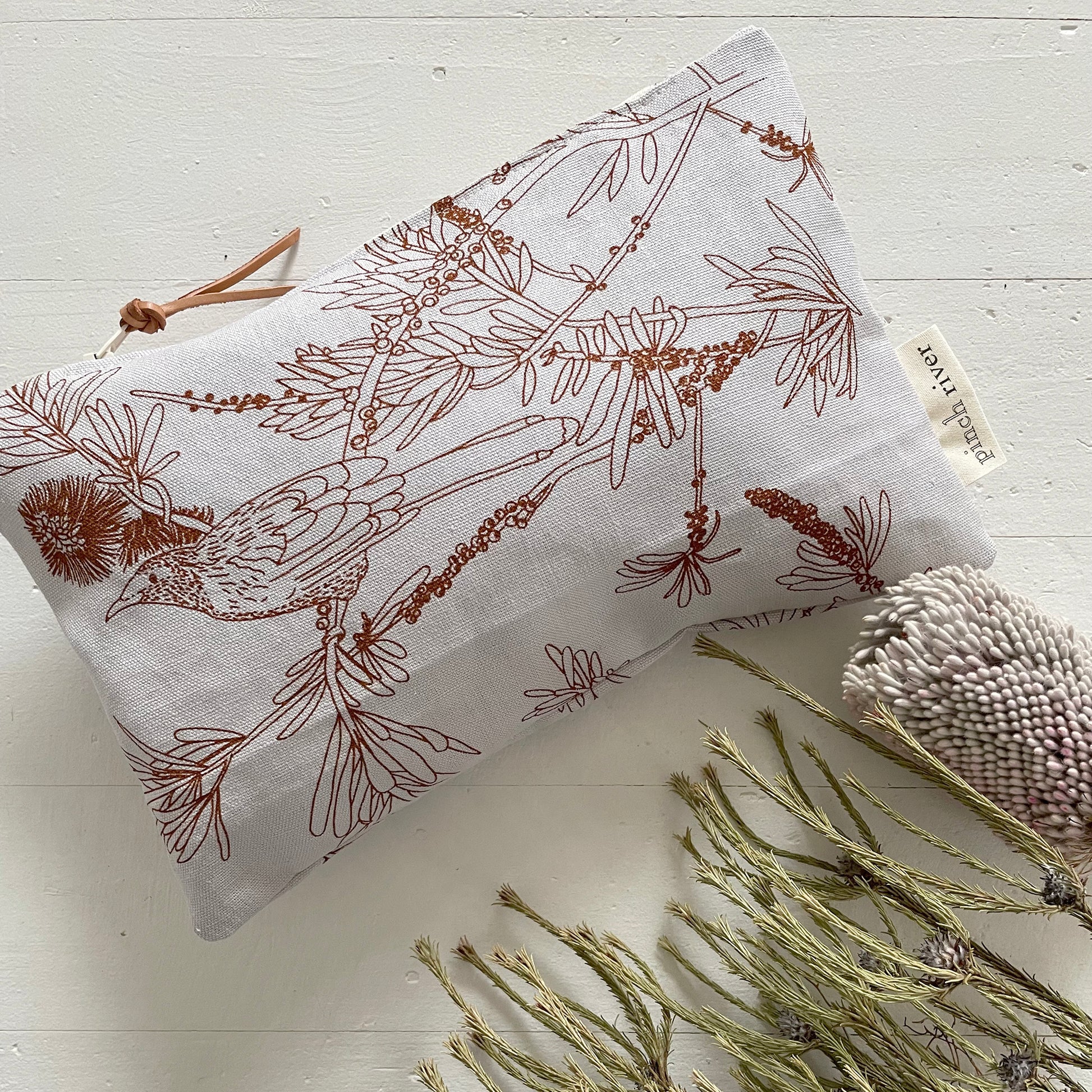 Pinch River zipper pouch featuring Wattle Bird print in Burnt Orange (colourway 2). Top view. Product image is styled with Australian native flora.